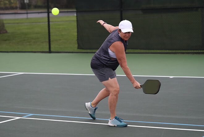 Elderly woman reaching for a backhand in pickleball