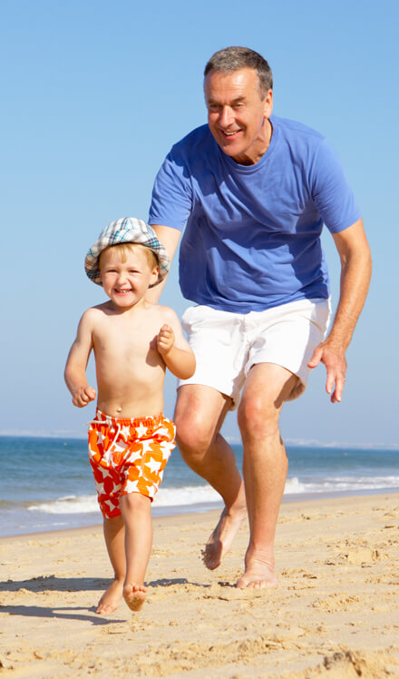 elderly man enjoying playing with his grandson on beach after receiving care from foot and ankle specialists