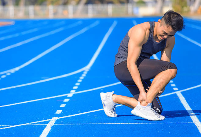 Young man suffering from sudden ankle and leg pain during the workout