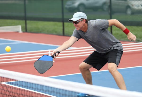 elderly man bending knees as he reaches for ball in pickleball game