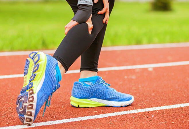 Athletic woman on running track has muscle spasm and touching hurt leg