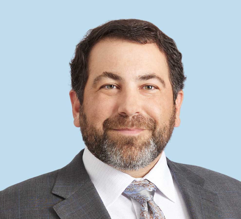 Aaron Koslin, DO professional headshot wearing gray suit and paisley tie