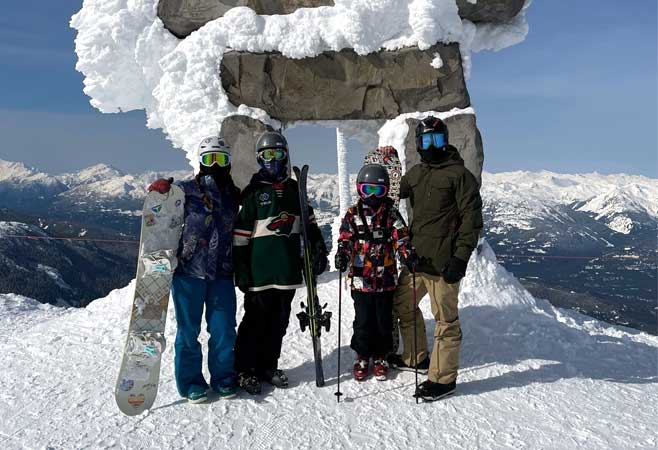 Dr. Christopher Baker snowboarding and skiing with family standing on a snow covered cliff