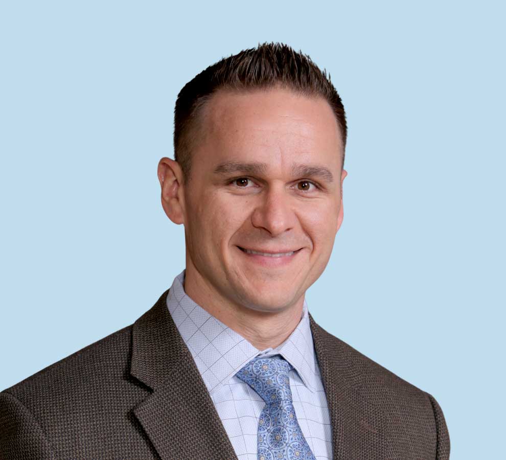 Christopher E. Baker, MD professional headshot wearing brown textured suit with blue paisley tie