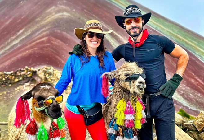 Ioannis Pappou smiling with wife, wearing cowboy hats posing with colorful festive llamas