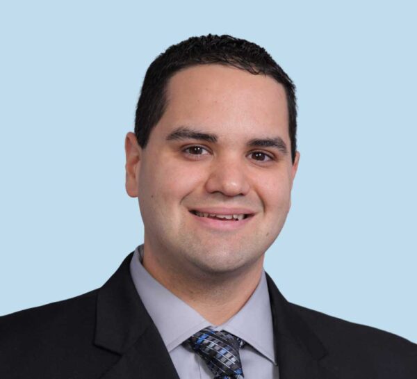 John D. Ramirez, DC professional headshot wearing black suit and dark patterned tie