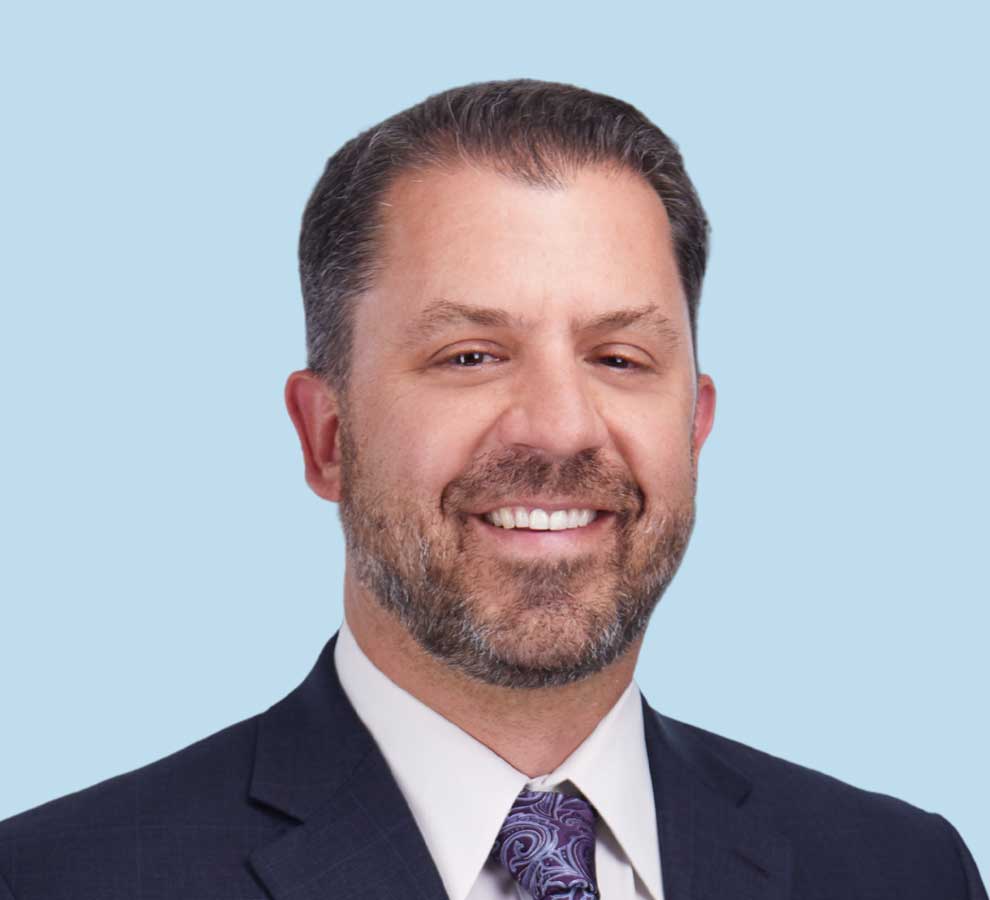 Michael A. Miranda, DO professional headshot wearing black suit and purple paisley tie