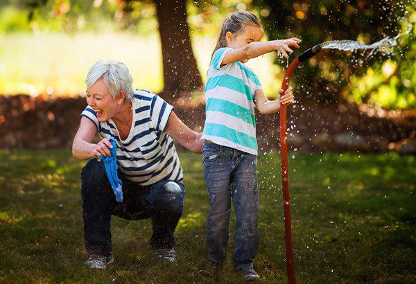 Grandmother playing with her granddaughter with the sprinkler