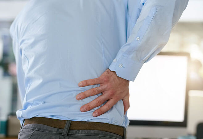 Rearview shot of a middle-aged businessman holding his back while standing at his desk