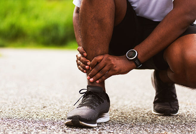 Closeup male holding sprained or broken ankle while running outdoors