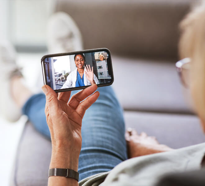 Woman sitting on couch receiving physician consultation via orthopedic telemedicine on mobile phone